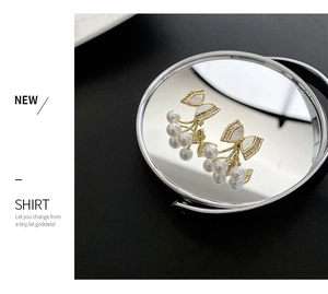 Close-up of golden bow earrings with pearl clusters displayed on a round mirror surface