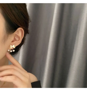 Detail of golden bow stud earrings with three white pearls shown on a female model