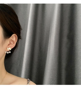Detail of bow-shaped gold pearl earrings worn by model with three dangling pearls
