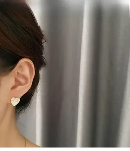 Detail von Herz-Ohrstecker mit Zirkon-Pavé und weißem Muscheleinleger am Ohr des Models