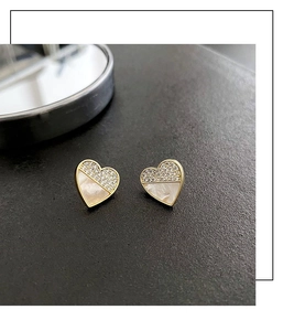Makro-Detail herzförmiger Gold-Ohrstecker mit schimmerndem Perlmutt und Zirkon-Besatz