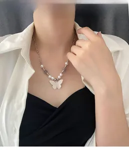 Detail view of a vintage butterfly pendant necklace with pearls and metallic chain on model