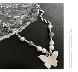 Macro detail of white butterfly pendant necklace with pearls and purple beads on stone