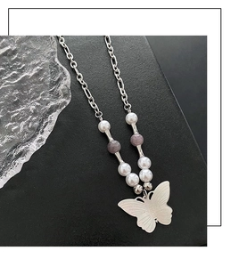 Detailed close-up of a silver butterfly pendant and beaded necklace chain in soft lighting