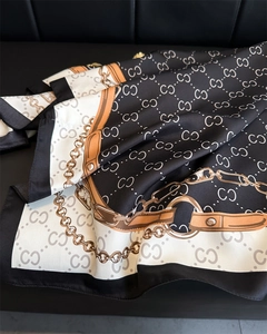 Close-up of silky printed scarf with gold chain patterns and luxury letter monogram