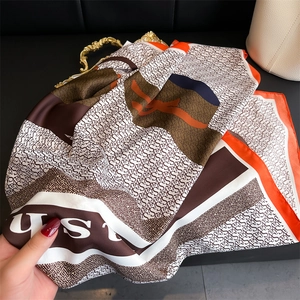 Detail of elegant silk scarf with orange and brown S-letter pattern on a gold tray