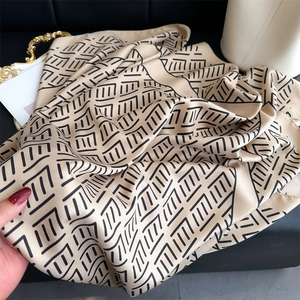 Detalle de un elegante pañuelo de seda beige con líneas negras junto a un bolso tipo cubo