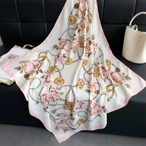 Détail d'un foulard en soie camélia avec chaîne dorée et imprimés roses sur satin