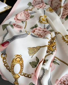 Détail d'un foulard en soie montrant des roses roses et des chaînes dorées sur ivoire