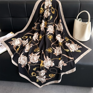 Détail d'un foulard en soie avec camélias et chaînes dorées drapé sur cuir noir