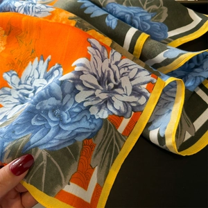 Detail of floral silk scarf showing orange and blue contrast colors with yellow rolled hem