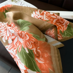 Macro detail of silk scarf showing orange flower print and brown striped edge on leather