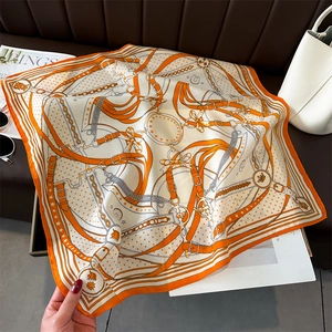 Detailed equestrian pattern on luxury orange silk scarf featuring stirrups and crowns