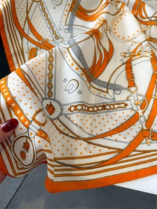 Detail of chain and horse head pattern on glossy orange silk scarf with drape effect