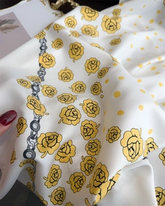 Detail of silk scarf with yellow roses, polka dots, and chain patterns on a white background