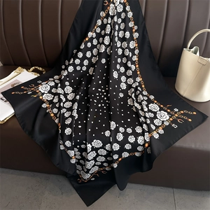 Detailed pattern of a black silk scarf with white roses and golden chain on a sofa