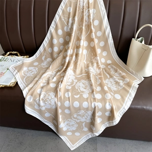 Elegant polka dot camellia silk scarf in beige styled on leather sofa with a handbag