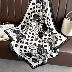 Detailed view of silk-like polka dot and rose pattern scarf on a leather sofa