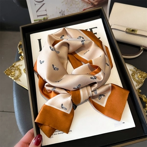 Detailed close-up of a luxury silk scarf featuring horse patterns and orange champagne tones