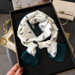 Silk-textured skinny scarf with horse head print tied in a bow on a black tray