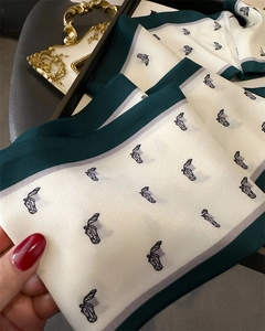 Detail of silk scarf showing horse print texture and dark green borders on creamy white fabric
