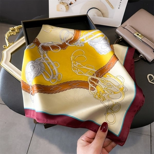 Detailed macro view of yellow silk scarf featuring equestrian belts and stirrup patterns