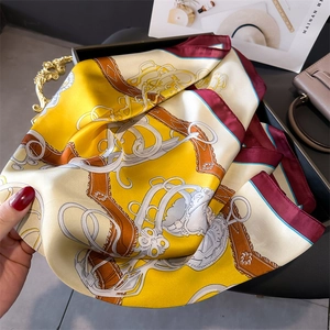 Detailed view of luxury silk scarf featuring golden chain and equestrian harness patterns