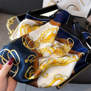 Detail of silk-like satin scarf with luxury chain horsebit print on golden tray