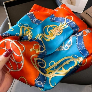 Detail showing the silky texture and golden chain print on an orange and blue scarf