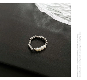 Macro shot of freshwater pearls and silver beads ring on a sleek black frosted background