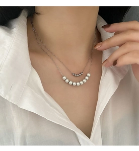 Detailed view of a double-layered necklace featuring silver beads and white pearls on a model