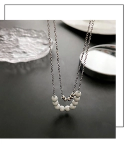 Close-up of double-layered silver necklace with delicate beads on a dark gray surface