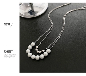 Detail of silver double-layer necklace featuring white faux pearls and metallic beads