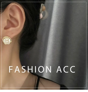 Close-up of a gold-tone round earring with a crystal-encrusted letter B on the ear