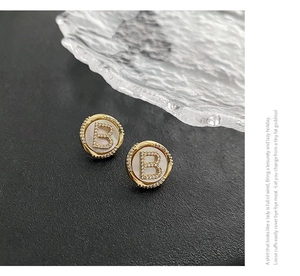 Detail of vintage gold-plated B-letter stud earrings with pavé crystals and mother of pearl