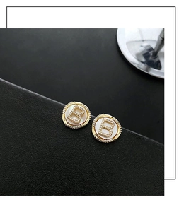 Macro detail of gold stud earrings with pave B letter and white mother of pearl inlay