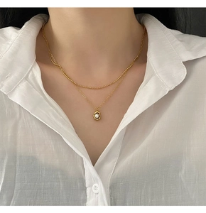 Détail d'un collier doré double épaisseur avec pendentif perle et chaîne perlée