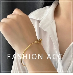 Detail of a minimalist gold bead-and-loop bangle worn elegantly on a female wrist