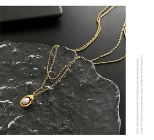 Détail d'un collier double rang doré avec pendentif perle sur une surface en verre