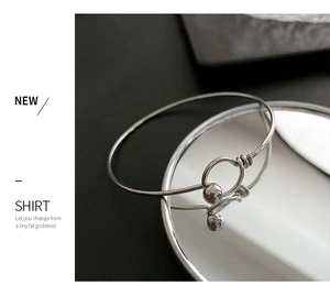 Macro detail of silver minimalist bangle featuring a spherical ball clasp on a mirror tray