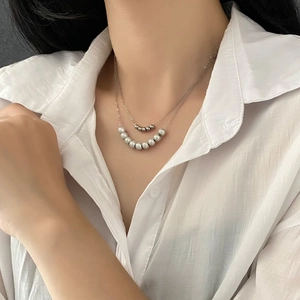 Double-layered silver necklace with metal beads and grey pearls on a female model