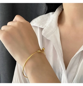 Detail of a minimalist gold bead knot bangle worn by a woman with a white linen shirt