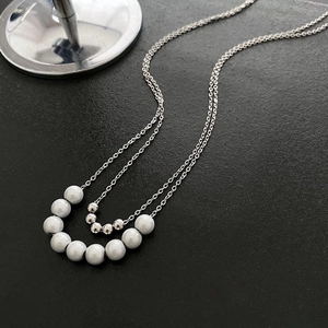 Minimalist double layer necklace with silver metal beads and white pearls on black texture