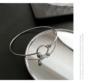 Macro shot of silver metal bangle with bead closure reflecting on a mirror surface