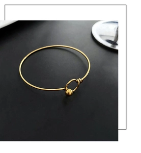 Close-up of a minimalist gold bangle with a unique ball-and-ring clasp on black surface