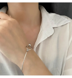 Close-up of a minimalist silver beaded bangle worn on wrist over a white shirt