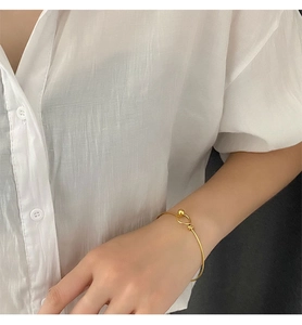 Close-up of a minimalist gold bead-clasp bangle on a wrist with white sleeve backdrop