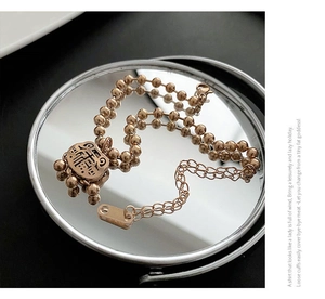 Detail of rose gold beaded bracelet with a hollow Fu lock pendant on a mirror