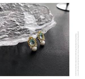 Detail of vintage gold earrings with light green gemstone and pearl drop