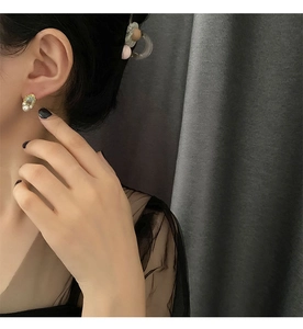 Detailed view of vintage gold stud earring with light blue stone and white pearl on model